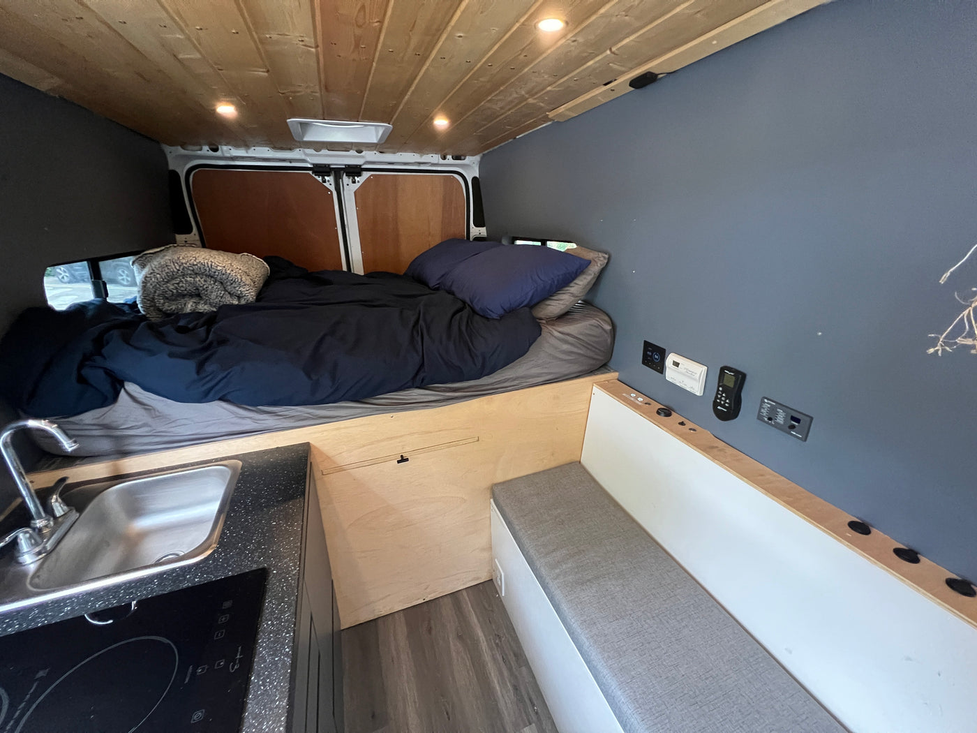 Inside this RV rental: wood-paneled ceiling, comfy bed, compact kitchen with sink, and wall-mounted controls. — photo 2