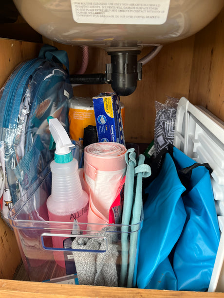 RV rental under-sink storage with cleaning supplies, foil, and trash bags neatly organized in a clear bin.