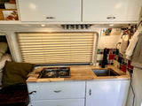 Interior of a compact RV rental kitchen featuring a wood counter, stove, sink, tiled backsplash, and upper cabinets.