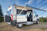 This light-colored rv rental camper van, parked outdoors with its side door open and awning extended, is ready for adventure.