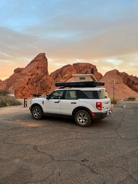 White Ford Bronco Sport with rooftop tent, a great RV rental for desert adventures among red rocks at sunset.