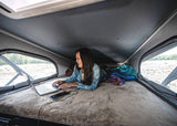 Remote work on the road in an RV rental. Woman with laptop & phone on a comfy bed inside a pop-top camper van.