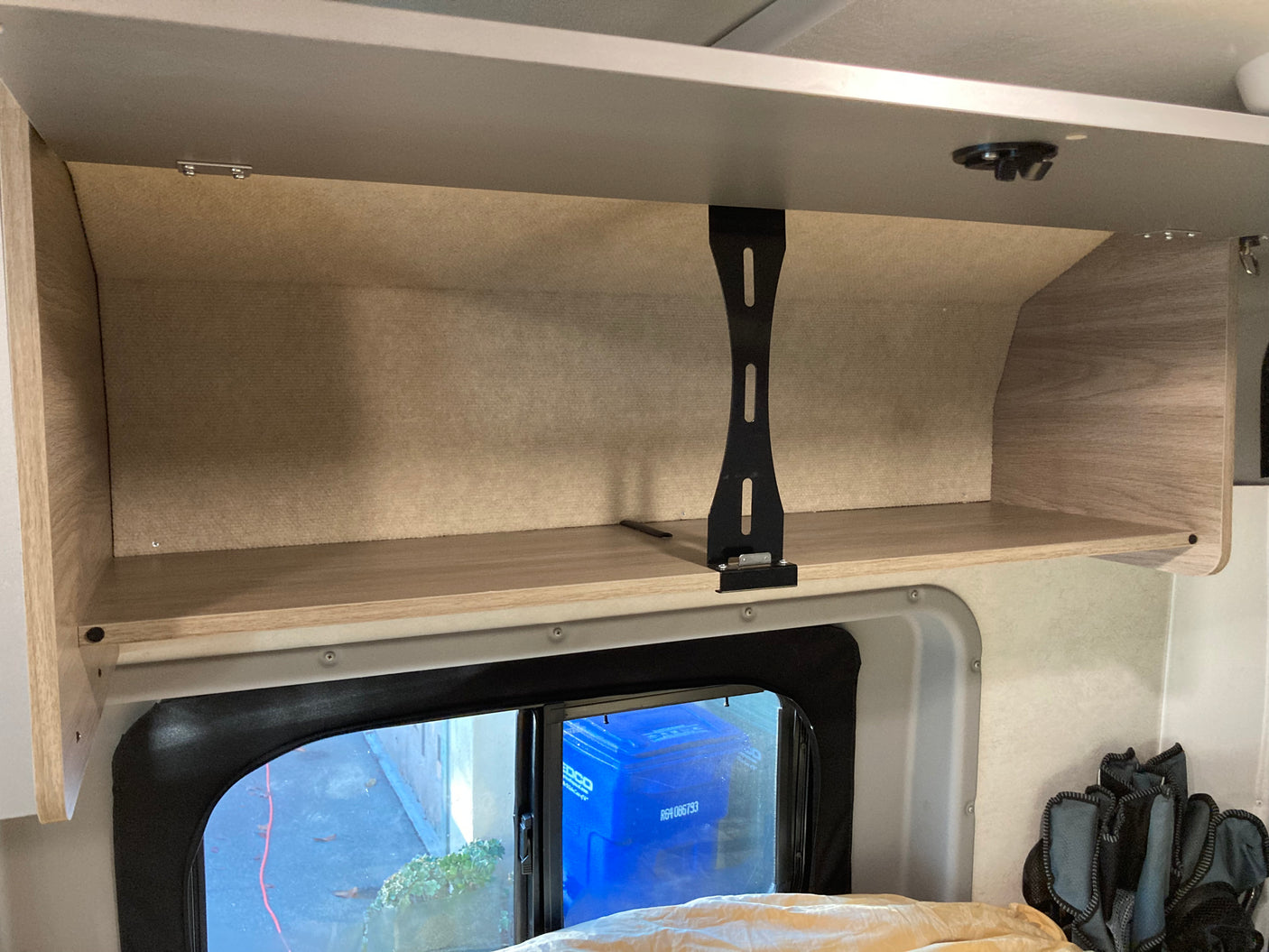 An rv rental's overhead cabinet and shelf, seen from inside, with a window below showing outdoors.