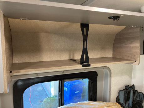 An rv rental's overhead cabinet and shelf, seen from inside, with a window below showing outdoors.