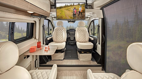 Luxurious RV rental interior features light quilted seats, a dining table, and mounted TV. Great for scenic travel.