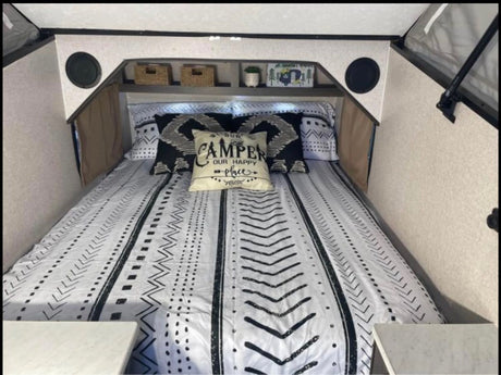 Cozy RV rental interior: A bed with black & white patterned bedding, throw pillows, overhead shelves, and built-in speakers.