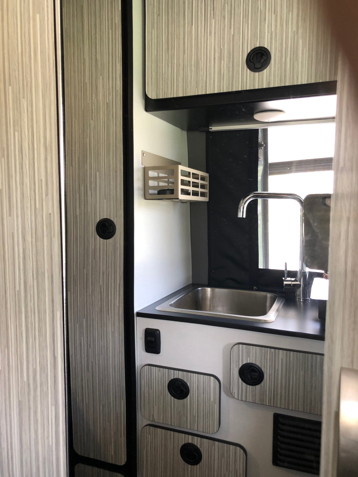 Modern RV rental kitchen featuring a stainless steel sink, chrome faucet, black countertop, and wood-grain cabinets. — photo 14