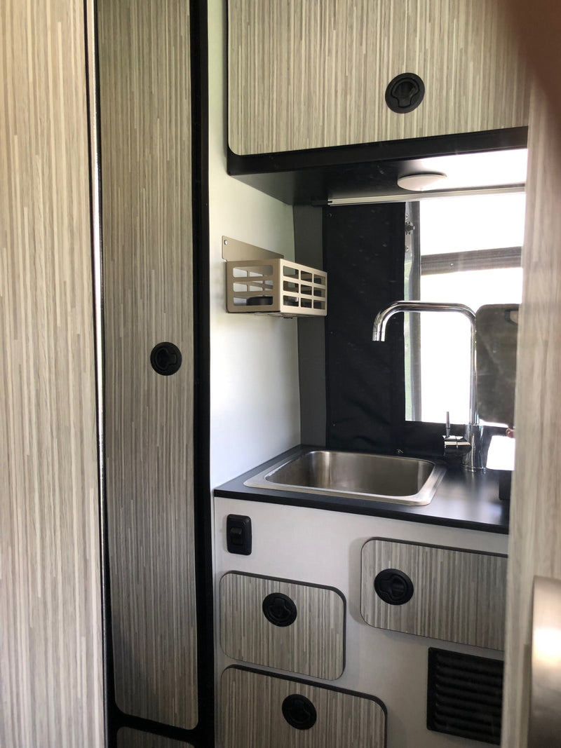 Modern RV rental kitchen featuring a stainless steel sink, chrome faucet, black countertop, and wood-grain cabinets. — photo 14