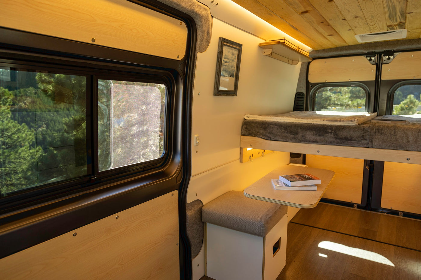 This inviting RV rental, a custom camper van, features a bed, dinette, and large windows with outdoor views. — photo 14