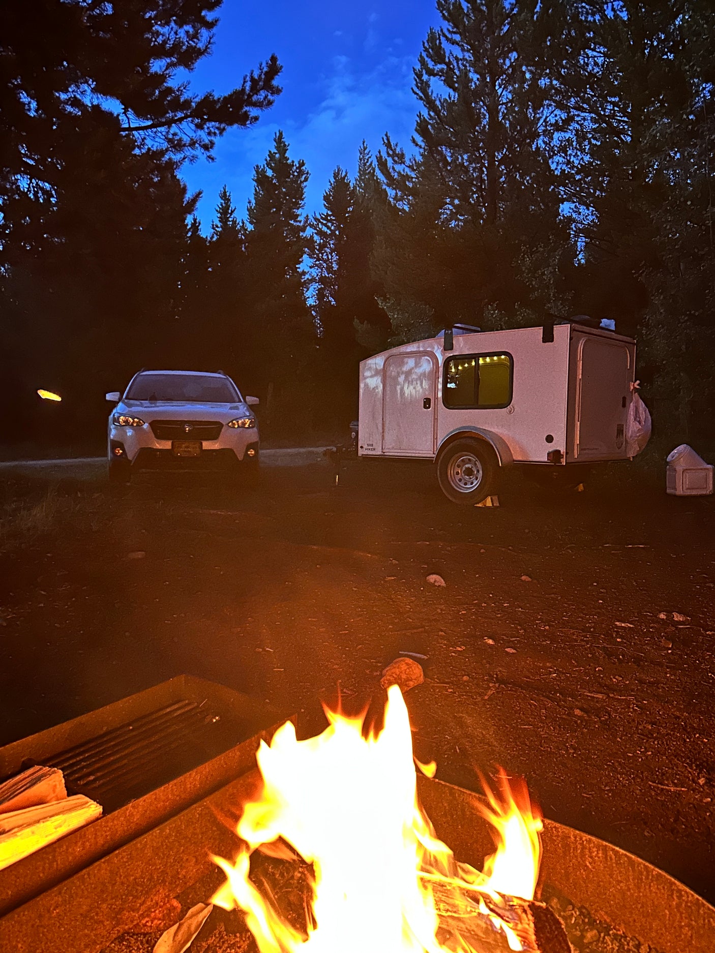 Campfire glows by RV rental teardrop trailer & car at night. Perfect for your outdoor adventure!