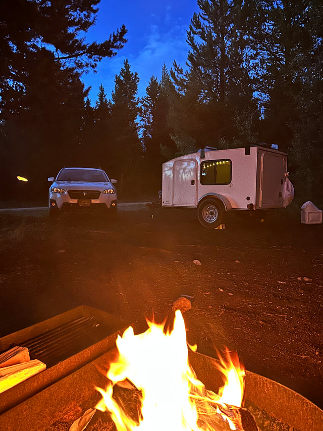 Campfire glows by RV rental teardrop trailer & car at night. Perfect for your outdoor adventure!