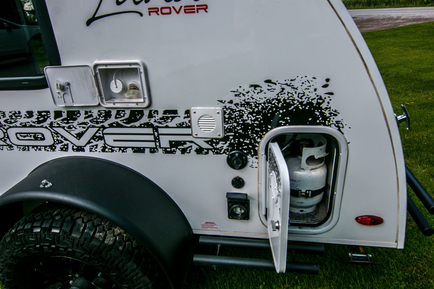 Side of an RV rental. Features include off-road tire, external hookups, and propane tank storage. Perfect for outdoor trips.