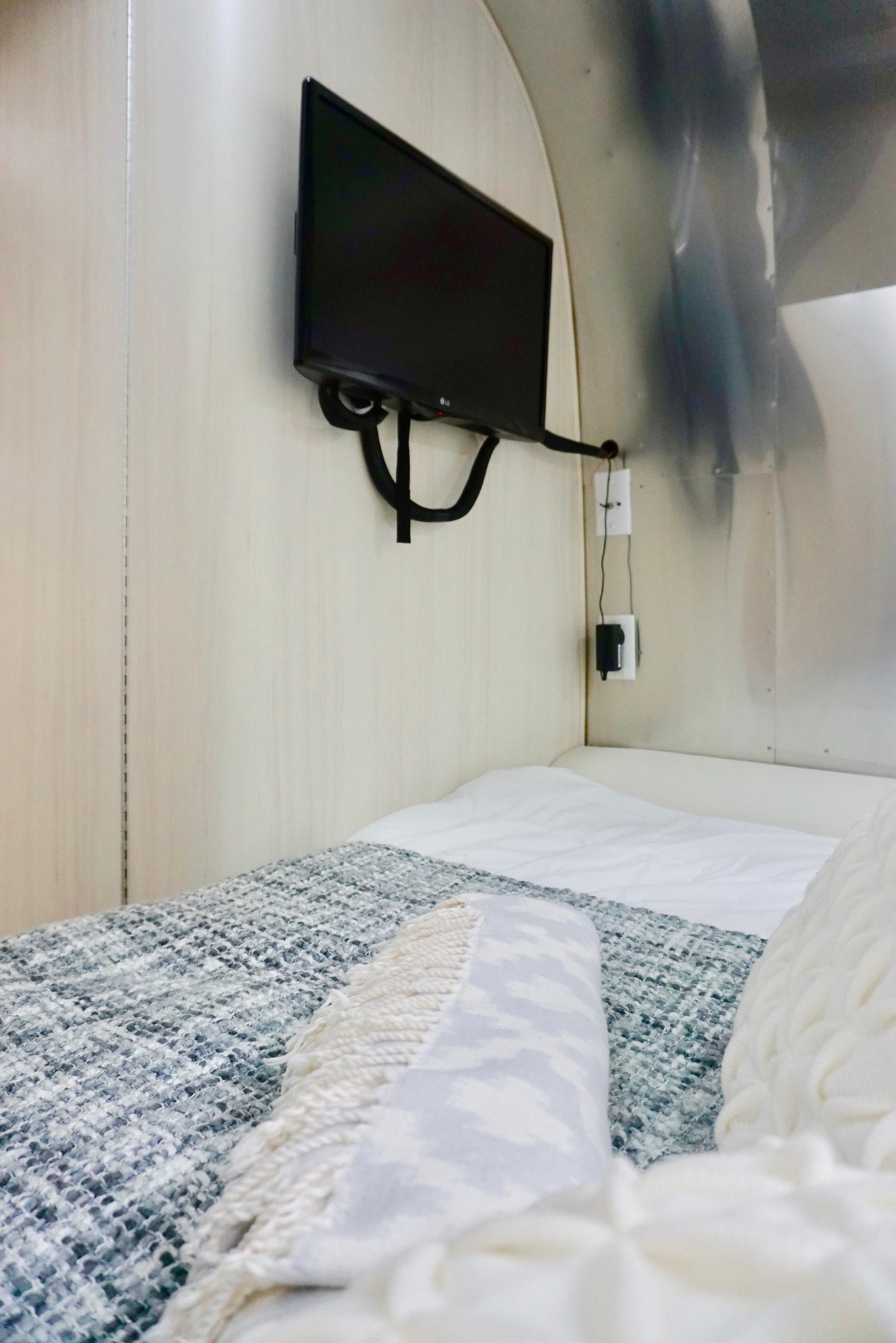 Cozy RV rental bedroom with wall-mounted TV, white sheets, and a textured blue/grey blanket for comfort. — photo 17