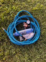 RV rental essentials: A blue RV water hose, inline water filter, and pressure regulator on grass, ready for safe camping.