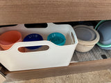 An organized RV rental drawer holds various plastic food storage containers and cups in a white bin.