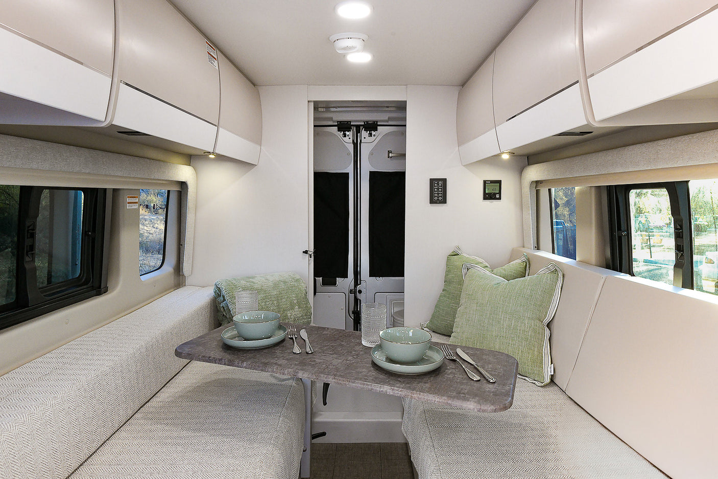 Spacious rv rental living area: A bright interior with opposite benches, a central table, overhead cabinets, and large windows.