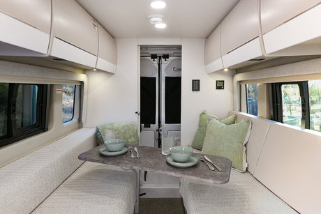 Spacious rv rental living area: A bright interior with opposite benches, a central table, overhead cabinets, and large windows.