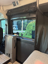 RV rental interior: a side window offers a view of another RV outside. Ceiling controls and floor-level power outlets are visible.