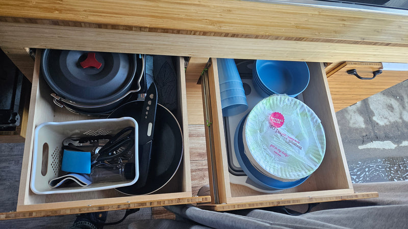 RV rental kitchen drawers stocked with camping pots, pans, bowls, cups, and paper plates, ideal for compact living. — photo 10