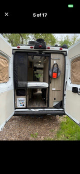 Inside an RV rental camper van with rear doors open, featuring a comfy bed, storage, and control panel. Perfect for your next trip.