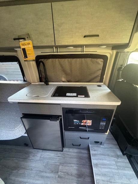 RV rental's compact kitchen: Sink, stovetop, fridge, microwave & overhead cabinets. Features solar power for adventure.