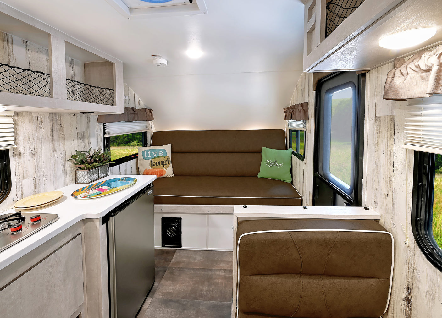 Bright RV rental interior with a functional kitchen, convertible sofa, and netted overhead storage. Perfect for road trips!