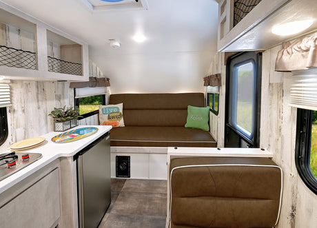 Bright RV rental interior with a functional kitchen, convertible sofa, and netted overhead storage. Perfect for road trips!
