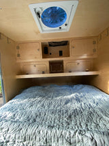 RV rental sleeping area: a plush bed, wooden cabinets & shelf, plus an overhead fan, creating a cozy interior.