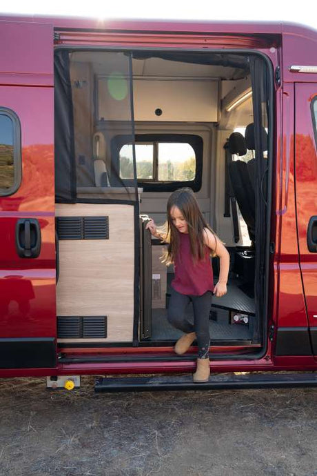 Young girl steps from a red camper van, revealing its cozy interior. An ideal rv rental for family adventures.