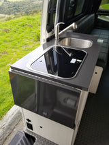 Modern **RV rental** galley kitchen with sink, cooktop, and folding counter, offering scenic outdoor views.