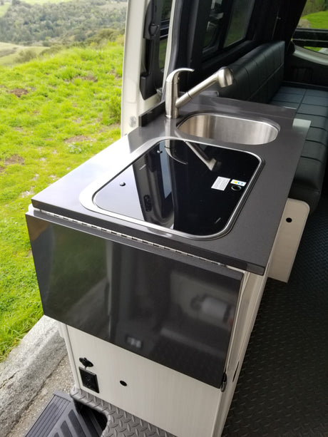Modern **RV rental** galley kitchen with sink, cooktop, and folding counter, offering scenic outdoor views.