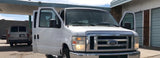 White Ford van with open doors parked near a grey van and storage units. Great for moving or an RV rental alternative.