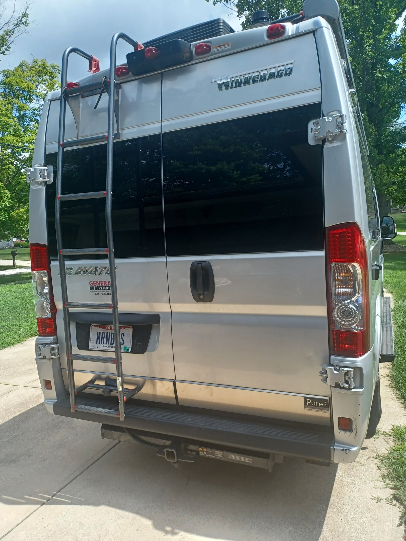 Rear view of a white Winnebago RV rental van, featuring a ladder, tail lights, and hitch. Ohio plate visible.
