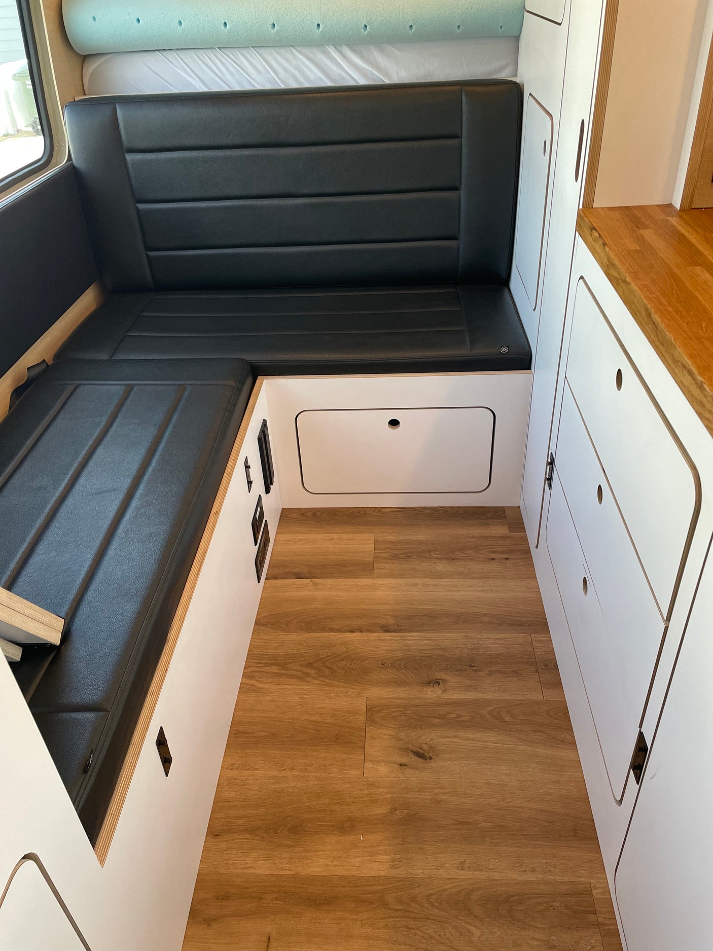 Modern camper van interior for **rv rental**, featuring sleek black seating, wood flooring, and smart white storage solutions.