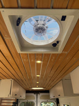 RV rental interior: Wooden plank ceiling, clear roof vent fan, recessed lighting, and practical white overhead storage cabinets.
