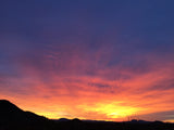 A vibrant desert sunset bathes silhouetted mountains in orange, yellow, & purple hues. Perfect scene for your RV rental.