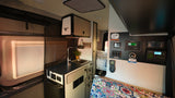 Inside this rv rental, a well-equipped camper van features a kitchen with sink, power control panel, and a patterned bed cushion.