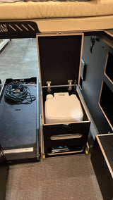 This RV rental's compact setup features a pull-out portable toilet, storage cubbies, and an organized cable drawer.