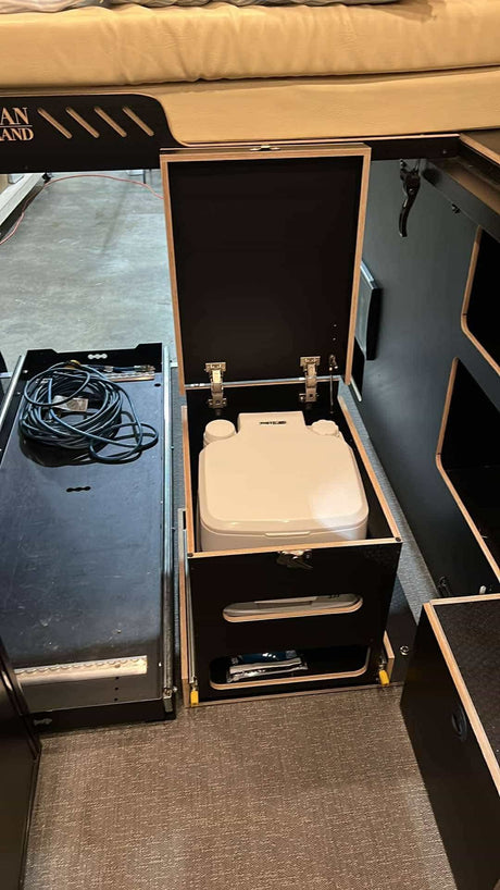This RV rental's compact setup features a pull-out portable toilet, storage cubbies, and an organized cable drawer.