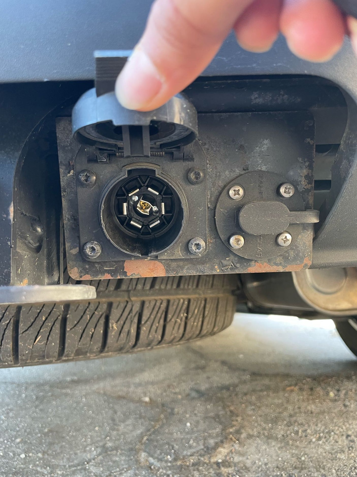 A hand opens a 7-pin RV electrical connector on a vehicle's rear. This is for trailer power, essential for any RV rental or towing.