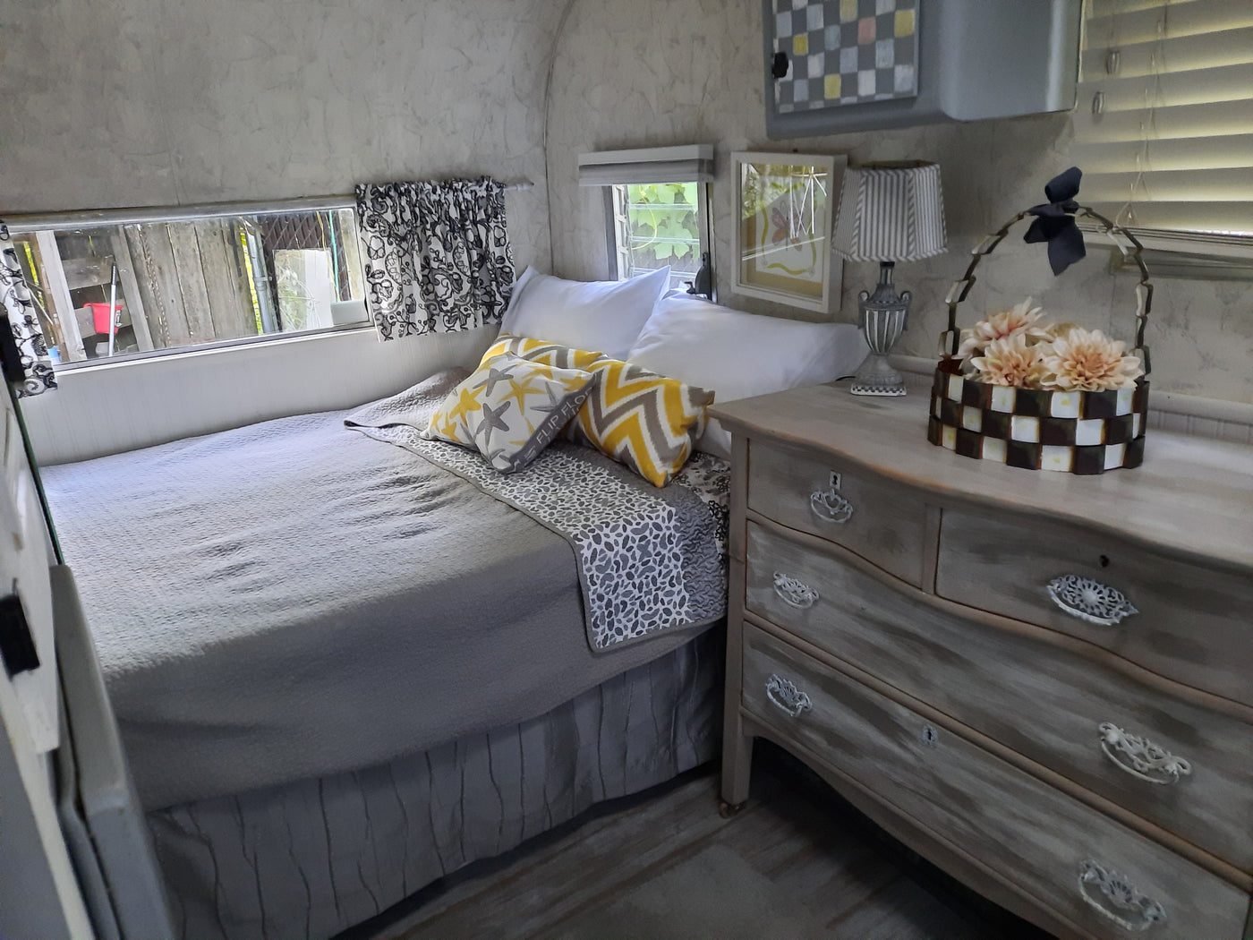 Inside a comfortable RV rental: a bedroom area with a grey bed, patterned pillows, distressed wood dresser, and unique lamps. — photo 4