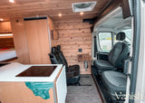 Detailed view of a modern RV rental interior, showcasing a compact kitchen, cedar walls, and versatile passenger seating.