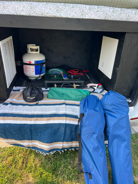 This RV rental's rear compartment stores a propane tank, camp stove, chairs, jumper cables, and a blanket.