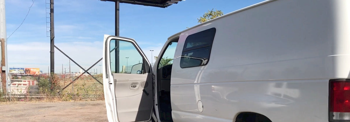White van, possibly an RV rental, with its door open near a large billboard structure under a clear blue sky. — photo 3
