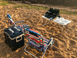 Beach day setup: colorful chairs, cooler, and portable stove with dinnerware on the sand, perfect for an RV rental trip.