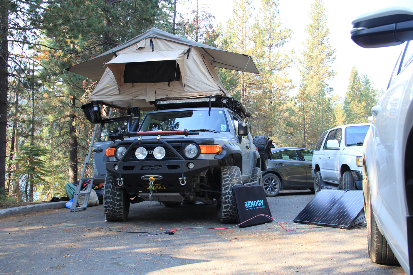 Grey off-road FJ Cruiser with rooftop tent & Renogy solar panel setup, offering RV rental-like comfort for forest adventures.