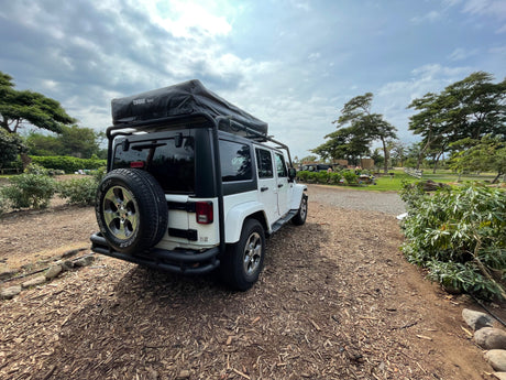 White Jeep Wrangler with Thule Tepui roof-top tent, a compact RV rental ready for outdoor adventures.