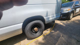 RV rental white van: Maintenance in progress. Rear wheel removed, exposing rusty hub. Yellow cable connected.