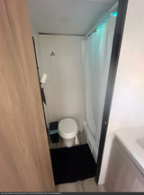Compact RV rental bathroom: toilet, shower with curtain, trash, & bath mat for a comfortable journey.