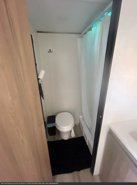 Compact RV rental bathroom: toilet, shower with curtain, trash, & bath mat for a comfortable journey.